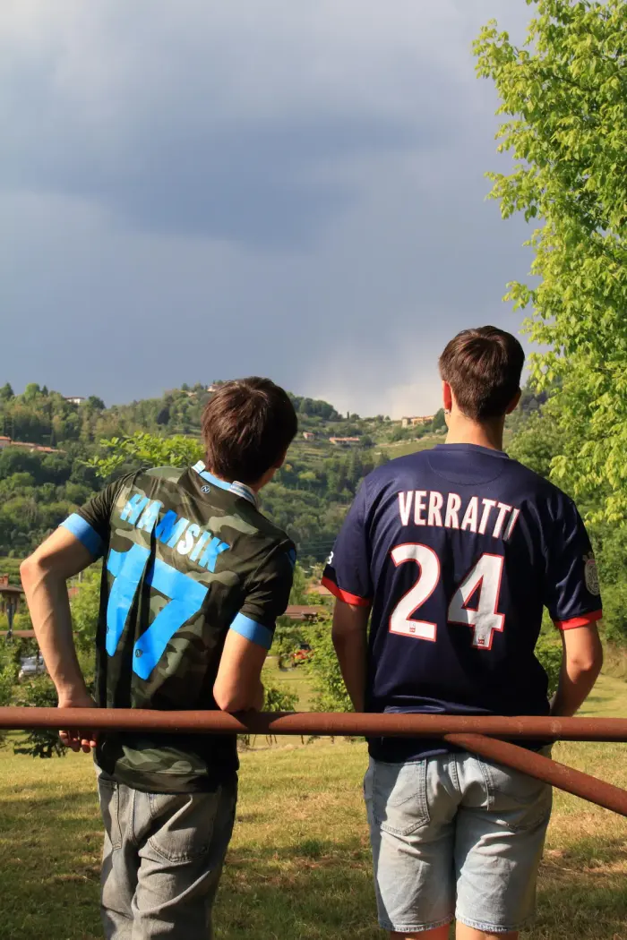 Two people seen from behind wearing football shirts, hills behind them